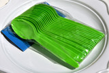 Green plastic spoons in a plastic packaging on a white plate in plastic