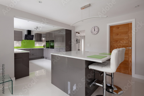 Fototapeta Naklejka Na Ścianę i Meble -  Contemporary fitted kitchen in striking lime green, grey and white colour scheme with built in appliances, white granite counter tops dual ovens island breakfast bar and hob