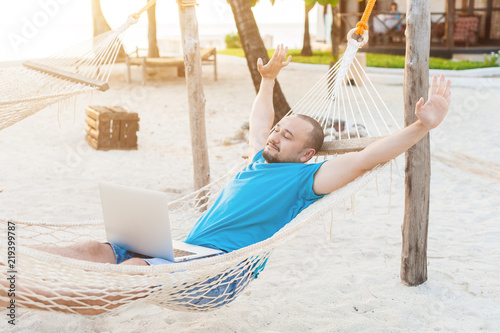 The man quite stretches lying in a hammock with a laptop. The concept of remote work