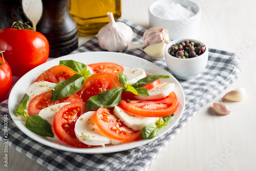 Photo of Caprese Salad with tomatoes, basil, mozzarella, olives and olive oil on wooden background. Italian traditional caprese salad ingredients. Mediterranean, organic and natural food concept.