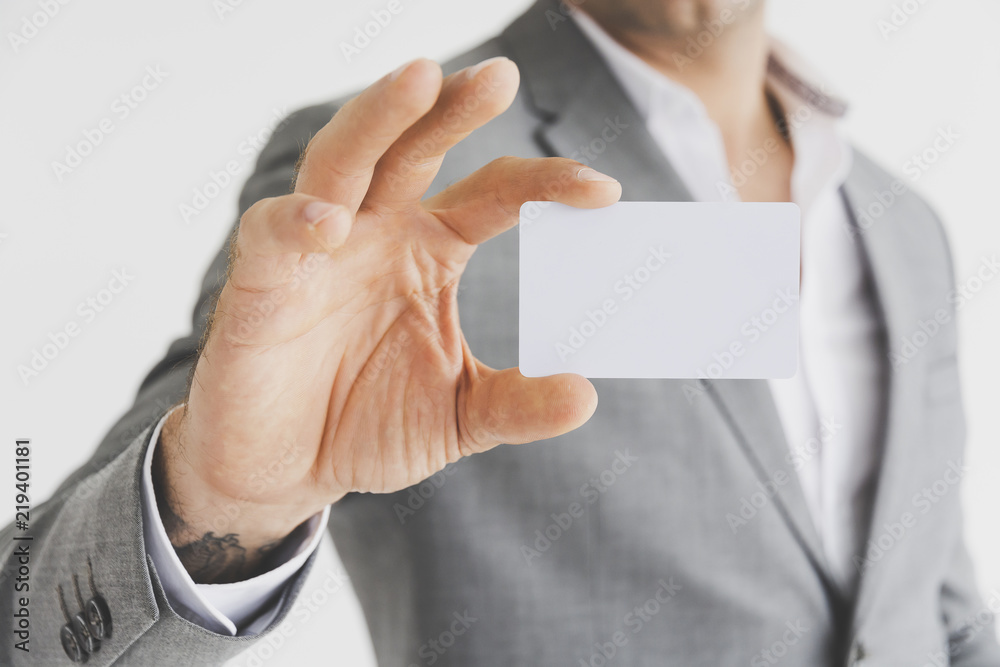 Man holding white business card or blank white credit card mockup front side view. Plastic bank-card design mockup on gray wall background. Man holding white business card or blank white credit card mockup front side view. Plastic bank-card design mockup on gray wall background.