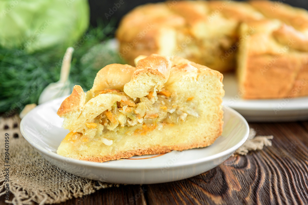 Homemade pie with cabbage, carrot, onion and meat on wooden background.