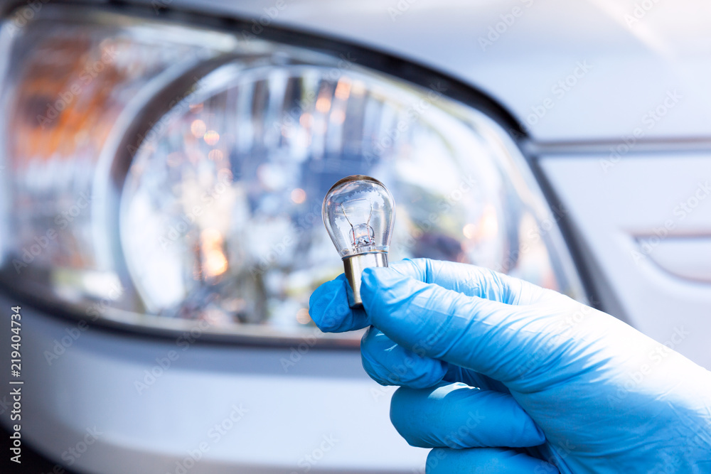 Close up of a light bulb with car headlight in the background - obrazy, fototapety, plakaty 
