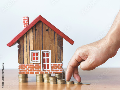 Fingers hand step forward on stack of coins ,wooden house model and step of coins stacks growing,saving and investment or family planning concept
