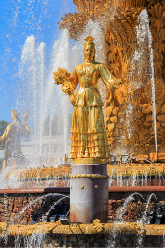 Gilded bronze girl against golden sheaf of wheat with technical hemp and sunflowers in fountain Friendship of peoples on VDNH in Moscow on a blue sky background