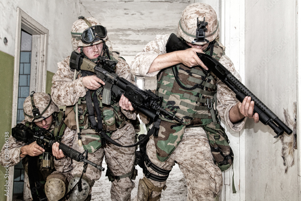 Obraz premium Marine assault team, counter-terrorism squad members, commando fighters in body armor, armed with service rifles, stalking through corridor to closed door, clearing rooms in abandoned city building