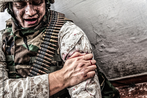 Fotografie Army soldier, commando fighter, marine machine gunner wounded in shoulder, clamping wound with healthy hand