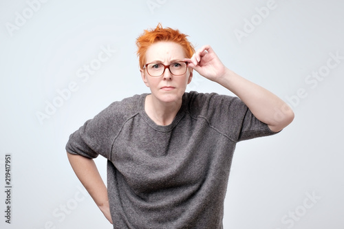 Surprised frustrated mature woman with red hair. She has problems with eyesight.