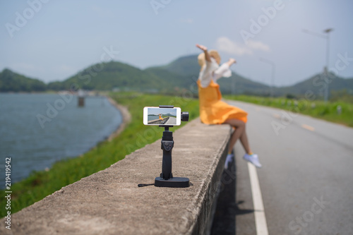 Young asian woman wearing yellow dress with camera standing on a dam and selfie a photo enjoy sunrise in the morning at Bang Pra Dam Chonburi Thailand.