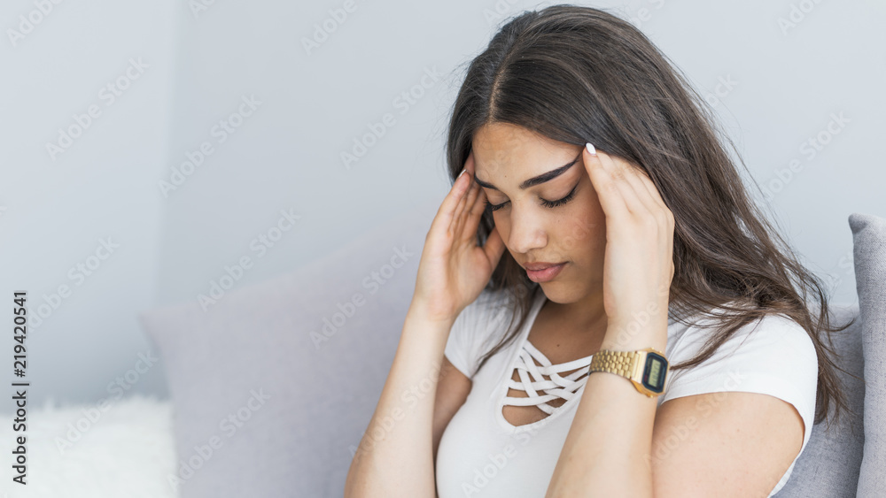 People, emotions, stress and health care concept - Unhappy young woman touching her head and suffering from headache People, emotions, stress and health care concept - Unhappy young woman touching her head and suffering from headache