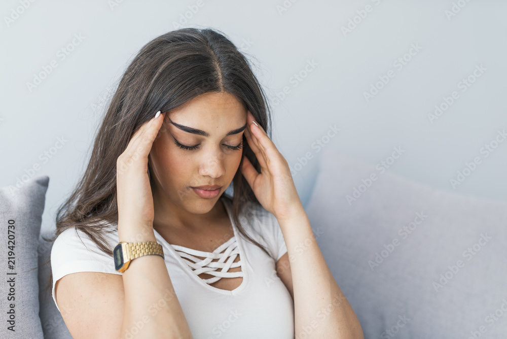 Portrait of beautiful young brunette with bare shoulders touching her temples feeling stress, on gray background Portrait of beautiful young brunette with bare shoulders touching her temples feeling stress, on gray background