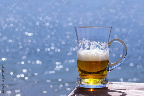 Mug of fresh beer on the table against the sea