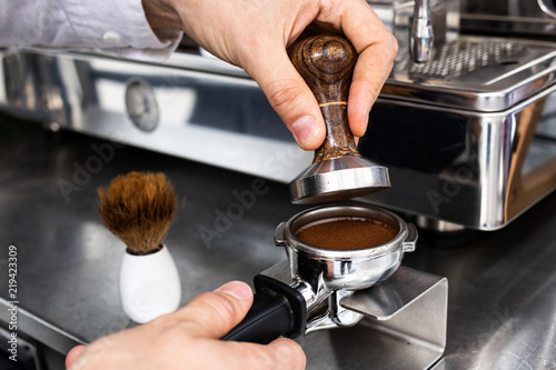 Barista pressing ground coffee into portafilter with a tamper. photo