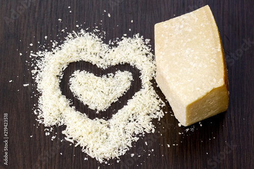 Pieces of hard cheese on black wood board. Top down of single tasty fresh yellow segment piece and finely grated cheese.