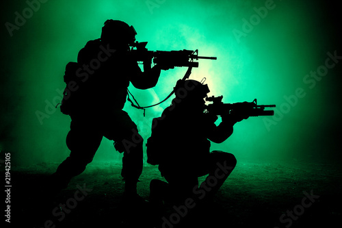 Silhouettes of two army soldiers, U.S. marines team in action, surrounded fire and smoke, shooting with assault rifle and machine gun, attacking enemy with suppressive gunfire during offensive mission © Getmilitaryphotos