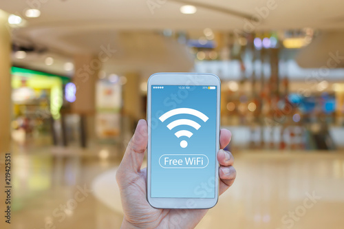 Hand holding smartphone with Free WiFi on screen over blurred in shopping mall background