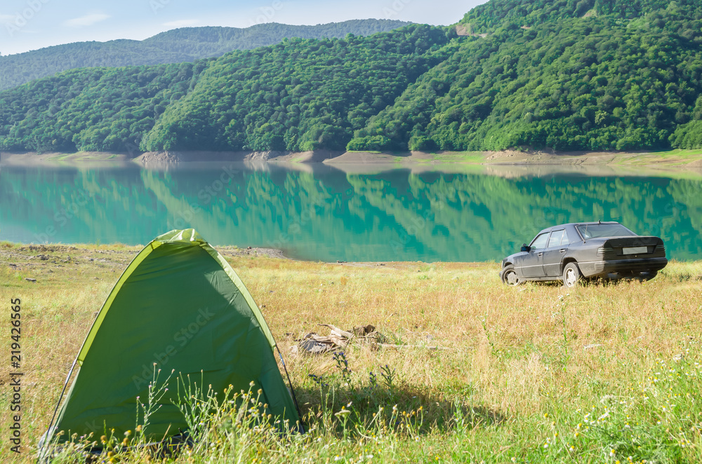 a tent stands on the shore of a beautiful pond surrounded by mountains