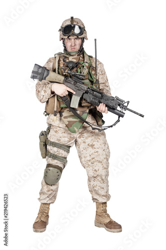Full length studio shoot of marine infantry, commando soldier in full protective ammunition, standing with service rifle equipped grenade launcher and looking at camera, isolated on white background