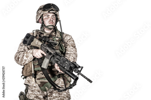 Studio shoot of marine infantry, commando soldier in full protective ammunition, standing with service rifle equipped grenade launcher and looking at camera, isolated on white background