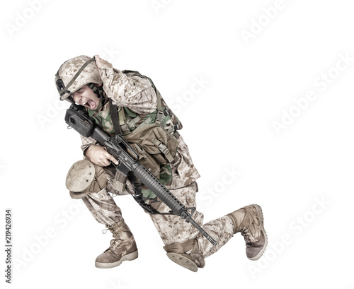 Army soldier in camo uniform, armed with assault rifle and machine gun, crouching to ground, holding helmets and covers ears with hands isolated on white studio shoot Grenade or bomb explosion