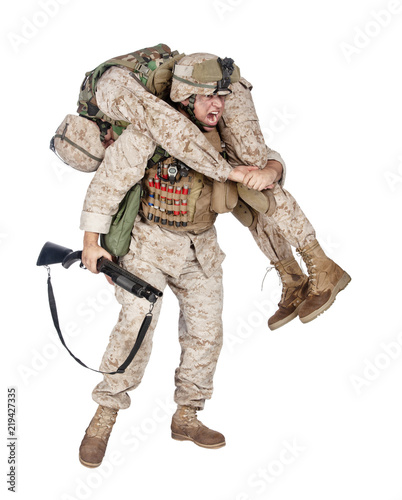 Obraz na plátně Army soldier armed with combat shotgun, carrying on back with firemans carry wounded and unconscious comrade