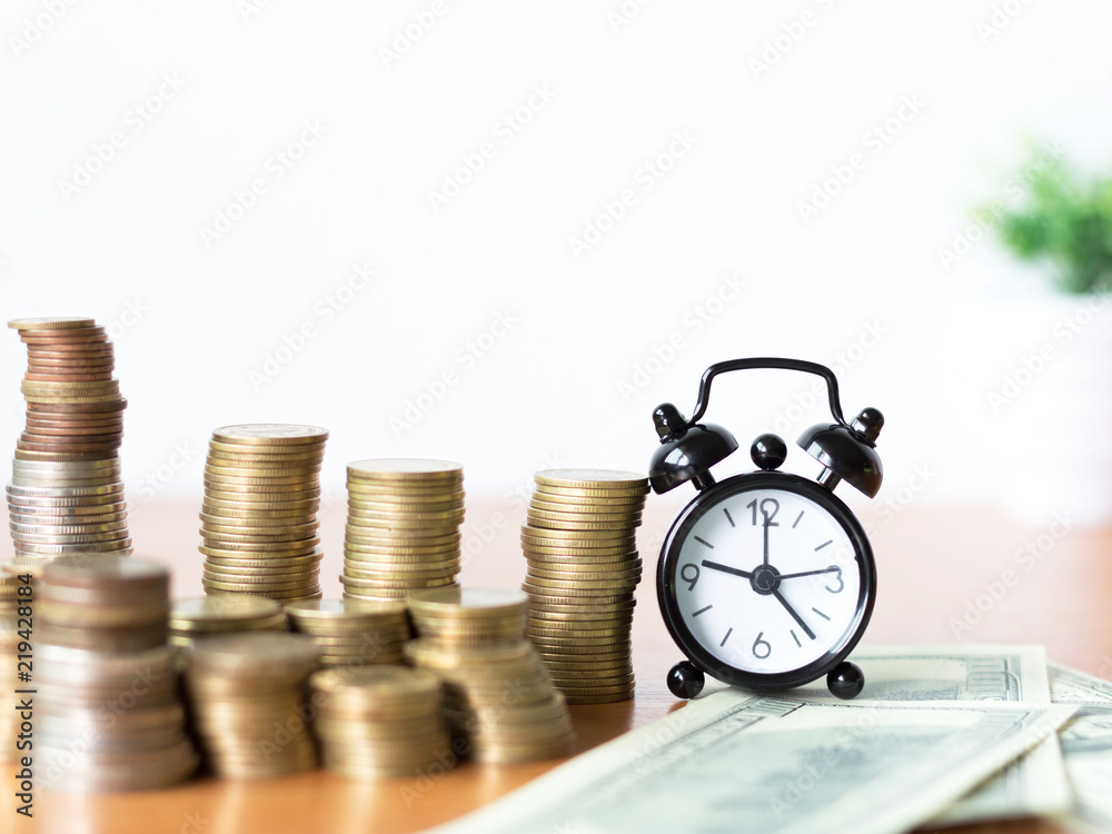 Alarm clock and stack of coins with money on wooden desk.finance and investment concept Alarm clock and stack of coins with money on wooden desk.finance and investment concept