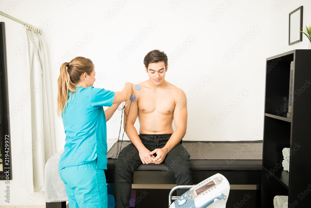 © AntonioDiaz - Physiotherapist Preparing Patient For Electrotherapy On Shoulder In Clinic