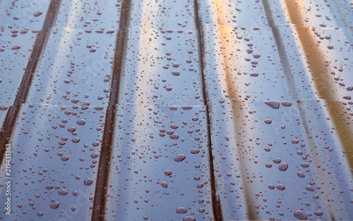 Fragment the brown metal roof of the house in the form of roof tiles with many drops after the rain top view close up