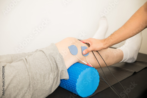Physiotherapist's Hand Positioning Electrodes On Patient's Knee photo