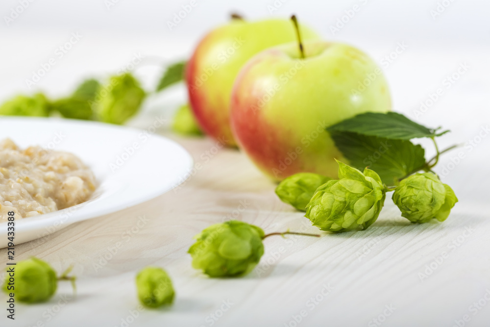 oatmeal porridge abundantly poured creamy melted butter on a white plate among apples and hops