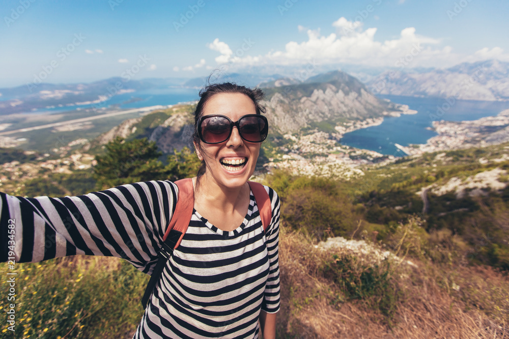 Naklejka premium Smiling young woman takes a selfie on background mountain and blue sea landscape horizon. View of the Bay of Kotor from the mountains Lovcen.