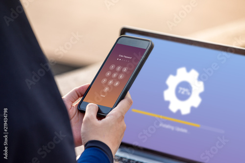 Hijab woman holding smartphone while entering the passcode with installing update on screen laptop background