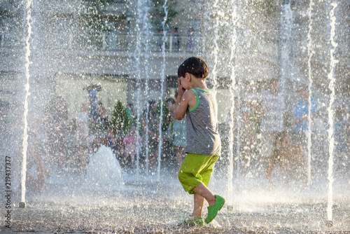 excited boy having fun between water jets  in fountain. Summer in the city