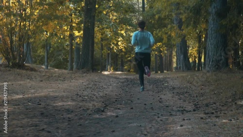 Teenager girl jogging in the forest on sunny summer day. Woman in leggings and sweatshot running along a path among the trees slow motion. photo