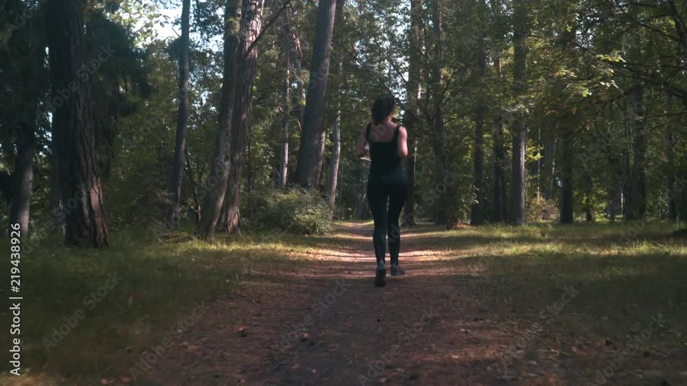 Sport girl running in city park on sunny summer day. Woman in leggings and sweatshot jogging along forest path among the trees Sport girl running in city park on sunny summer day. Woman in leggings and sweatshot jogging along forest path among the trees