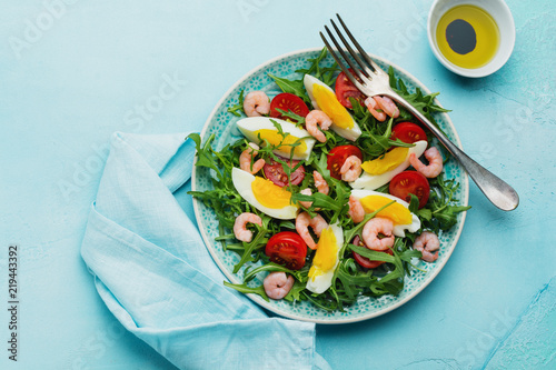 Arugula, cucumber, tomato, eggs and shrimp salad with soy sauce on ceramic plate. Selective focus. Top view.