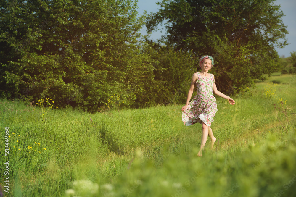 A cute cheerful young girl in a light cotton dress strolls along the country road against the backdrop of summer greenery at sunset A cute cheerful young girl in a light cotton dress strolls along the country road against the backdrop of summer greenery at sunset