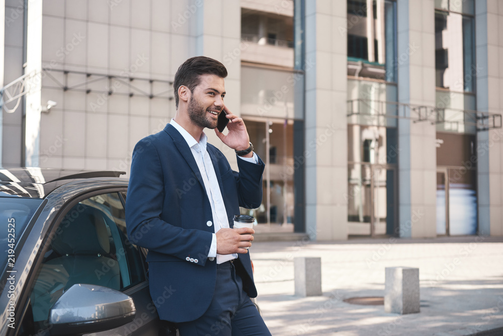 Handsome young businessman in a big city, talking on the phone and drinking coffee Handsome young businessman in a big city, talking on the phone and drinking coffee