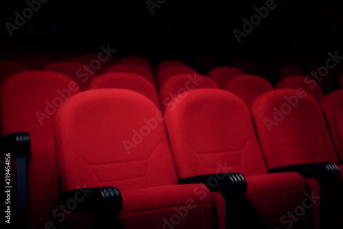 Many rows of red velvet seats in a cinema or theater stage, in semi-darkness. 