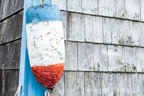 vintage blue, white and red lobster buoy hanging on the corner of a weathered fishing shack in Massachusetts photo