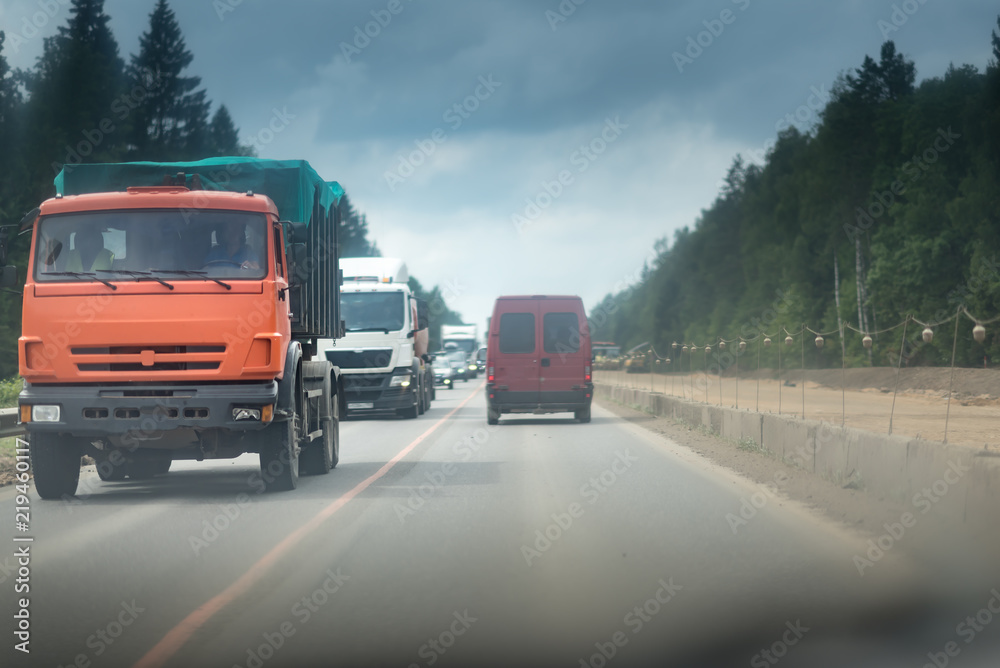 A lorry and truck on the road with concrete white and red blocks from one side and safety rail or barrier from other side. Part of the highway is under construction