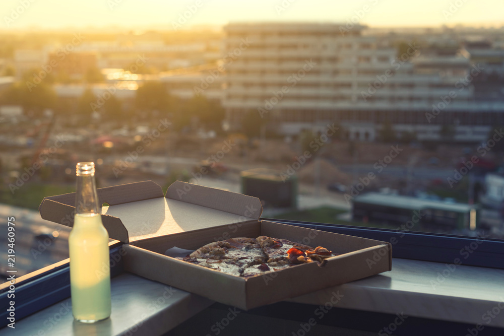 huge pizza in a box with a bottle of mojito on the sunset city background