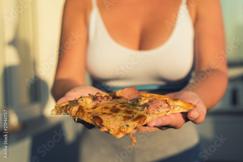 A girl in a sports suit holds a huge piece of pizza. Concept