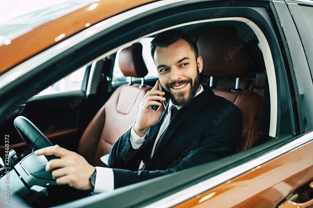 Happy businessman talking on the phone in car while driving on city