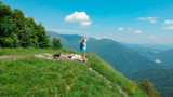 AERIAL: Woman hikes up to the top of mountain and lifts her arms in the air.