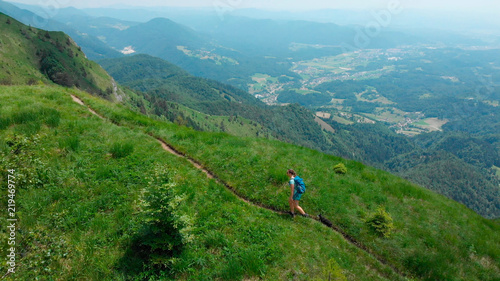 AERIAL  Cute little dog and active female owner hike up a narrow mountain path.