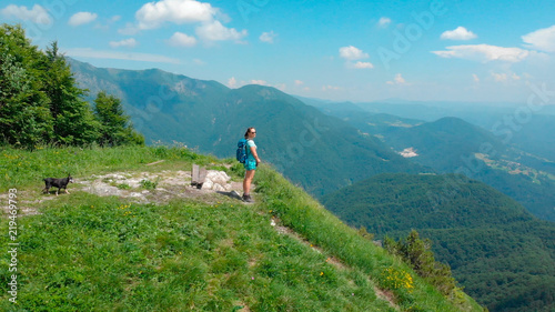 AERIAL: Cheerful young woman looks at the spectacular valley from mountaintop.