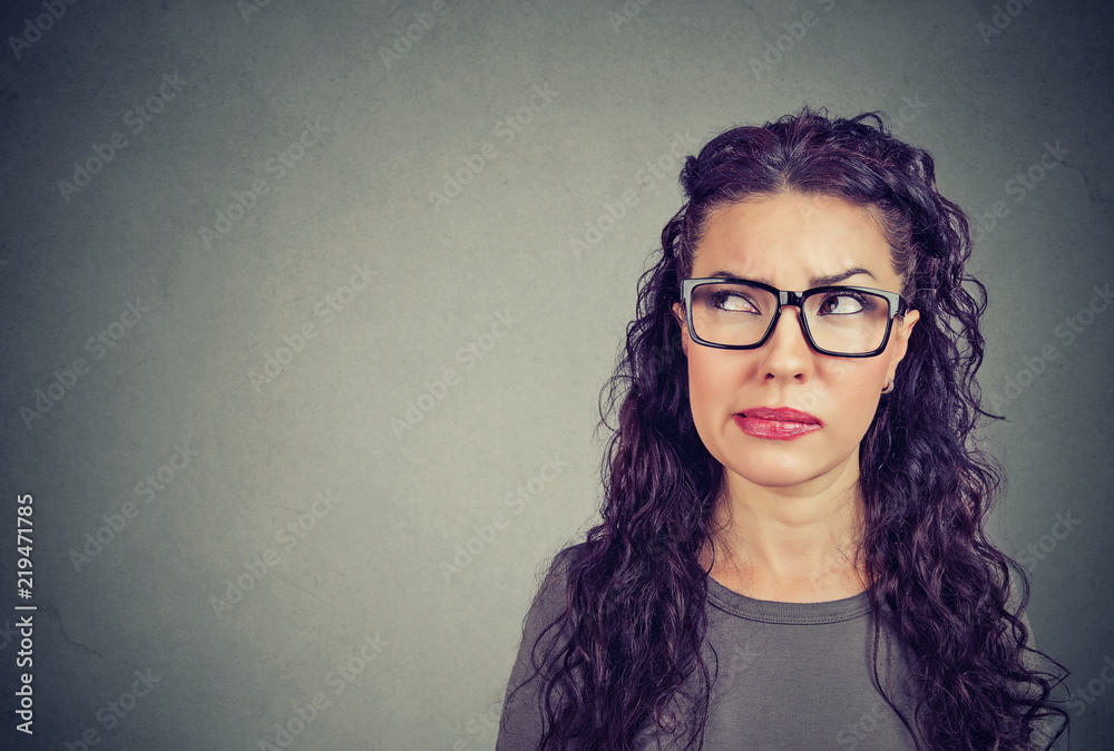 Closeup of a thoughtful young woman in glasses looking up contemplating