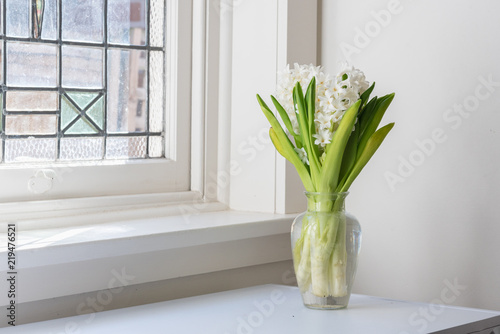 White hyacinths in glass vase on table next to vintage window (selective focus)