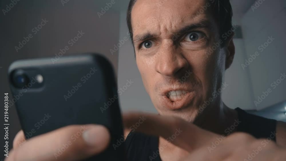 Angry man aggressively uses smartphone at home in the kitchen.